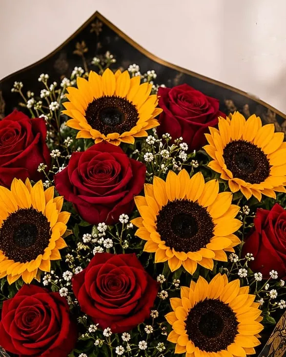 Detalle: ramo grande de rosas rojas y girasoles con paniculata en papel negro con detalles dorados y cinta roja