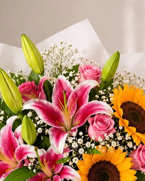 Detalle: ramo de lilium rosados, girasoles y rosas rosadas con paniculata en papel blanco con cinta rosada