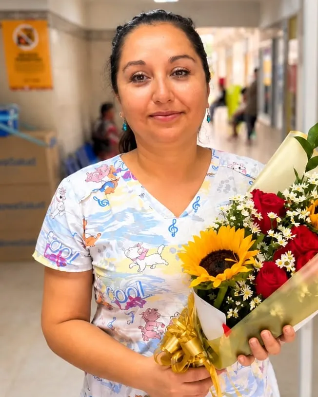 Mujer en un pasillo de clínica con un ramo de rosas rojas y girasoles